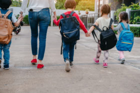 children with mother and backpacks walking hand in hand