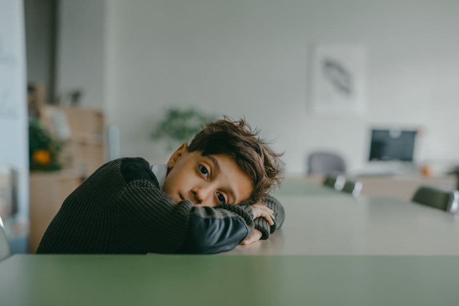 A primary-school child gazing away from an open workbook at the kitchen table, struggling to concentrate on homework.