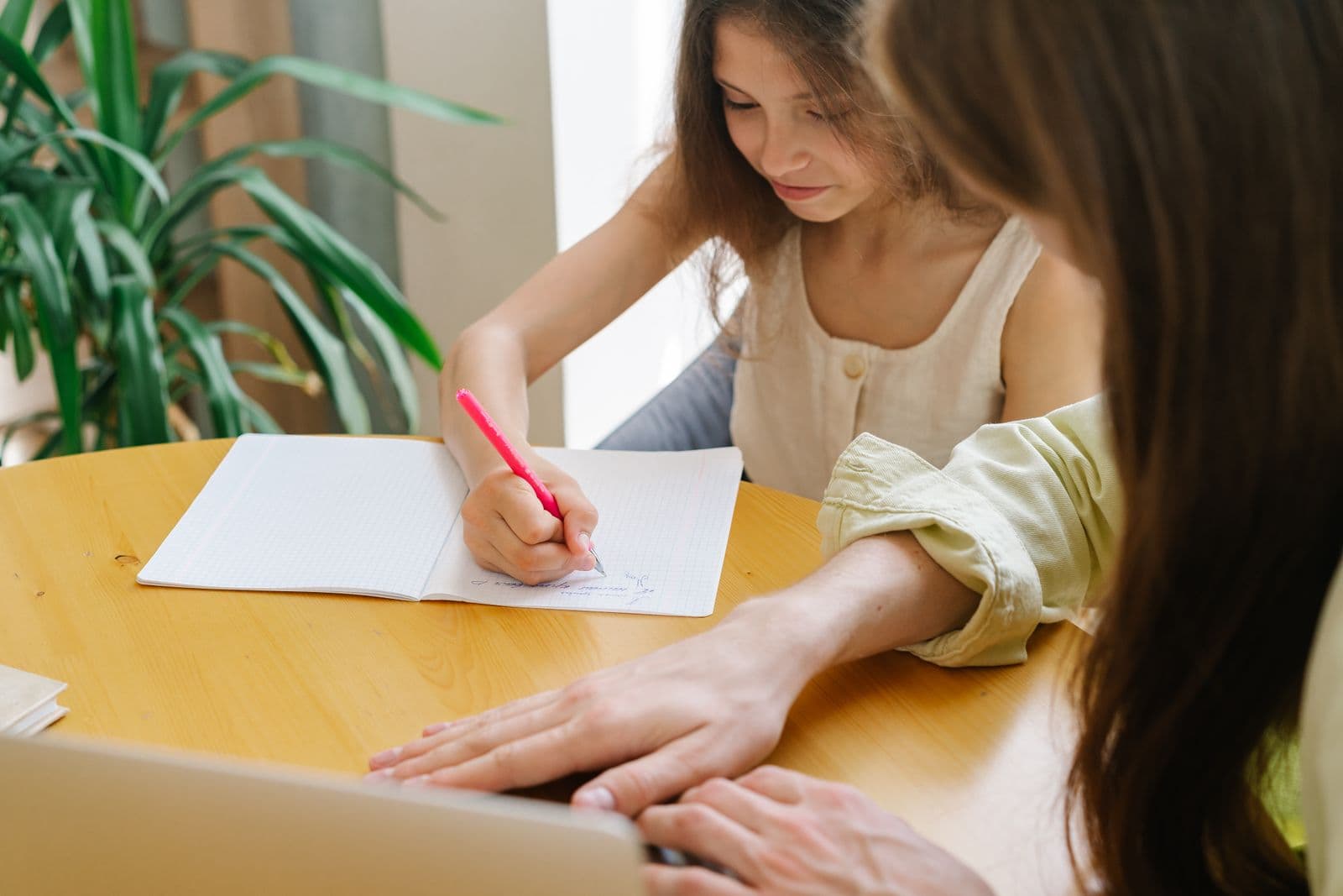 A child writing in a notebook while a parent sits beside them, helping calmly.