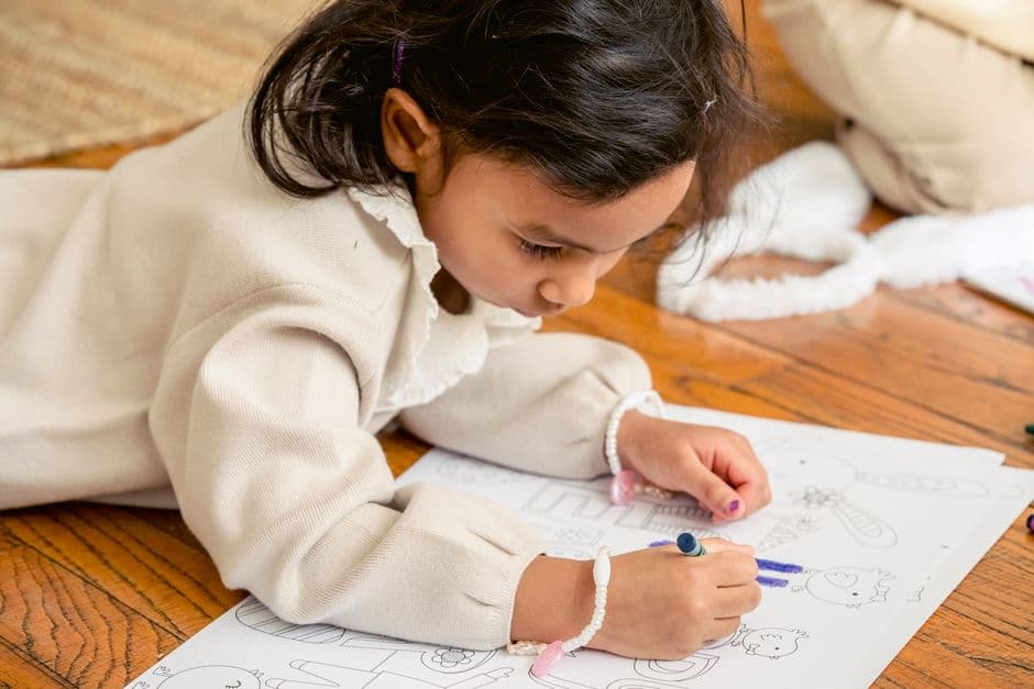 A young child in the year before school, sitting on the floor happily looking at a picture book.
