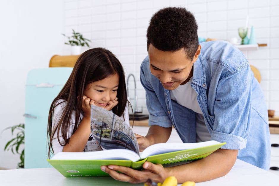 A parent and their primary-school child sitting together at a kitchen table, calmly reading a printed school report.