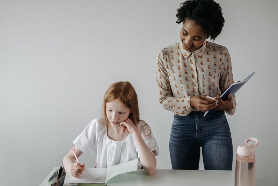 An educator sitting beside a primary-school child, working through a page at the child's own level.
